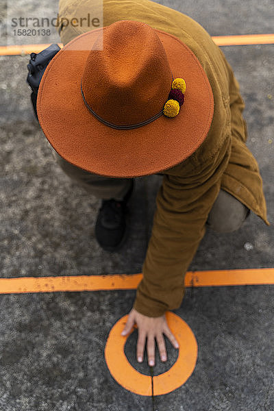 Draufsicht eines Mannes mit Hut,  der seine Hand auf einen Kreis auf dem Boden legt