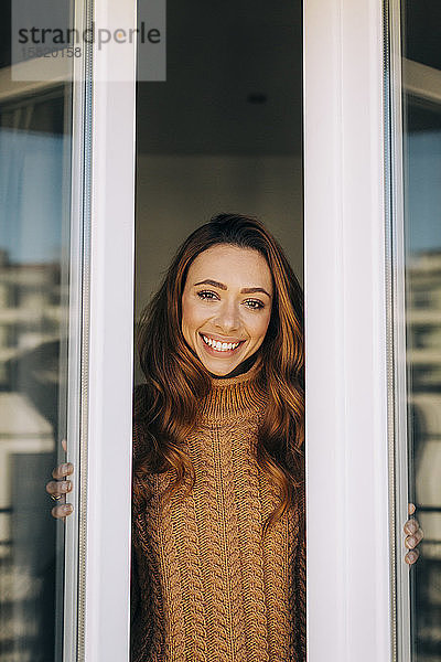 Porträt einer glücklichen jungen Frau am Fenster