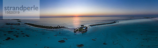 Malediven,  Hubschrauberansicht der Bungalows des Touristenresorts,  die sich bei Sonnenuntergang entlang der Küste der Insel Maadhoo erstrecken