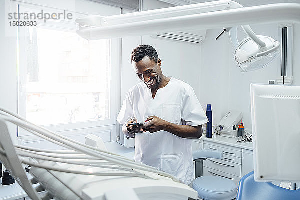 Glücklicher Zahnarzt benutzt Handy in seiner Praxis
