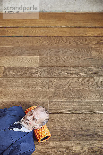 Älterer Geschäftsmann entspannt sich auf Holzboden,  ruht auf Faszienrolle