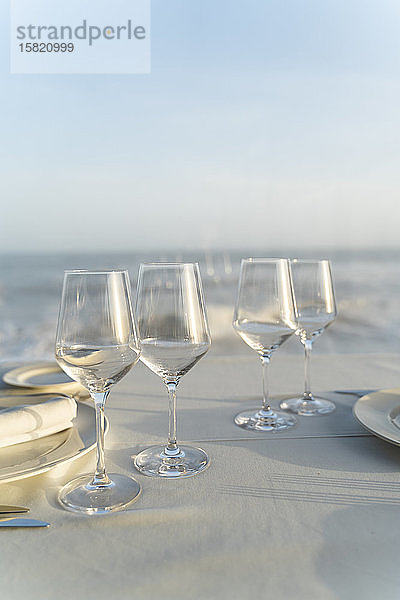 Spanien,  Leere Weingläser auf gedecktem Restauranttisch mit Meer im Hintergrund