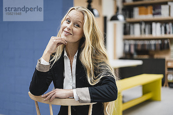 Porträt einer lächelnden jungen Geschäftsfrau,  die auf einem Stuhl im Loft-Büro sitzt