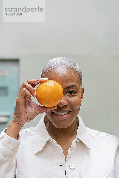 Porträt einer glücklichen Frau,  die im Freien ihr Auge mit einer Orange bedeckt