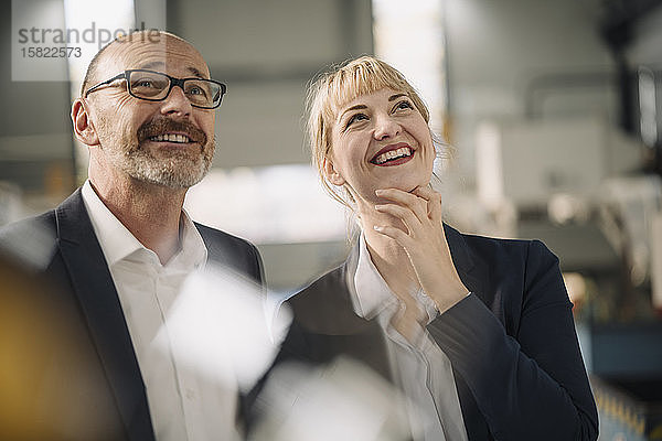 Porträt eines glücklichen Geschäftsmannes und einer glücklichen Geschäftsfrau in einer Fabrik mit Blick nach oben
