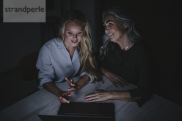 Mutter und erwachsene Tochter schauen im Dunkeln auf den Laptop auf dem Tisch
