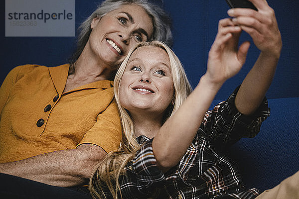 Glückliche Mutter und erwachsene Tochter,  die auf der Couch ein Selfie machen