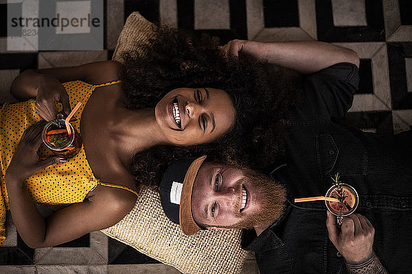 Porträt eines glücklichen Paares,  das auf dem Boden liegt und frischen Eistee trinkt