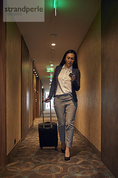 Geschäftsfrau auf dem Hotelkorridor mit Rollkoffer