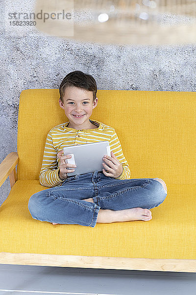 Junge spielt mit Tablette auf gelber Couch
