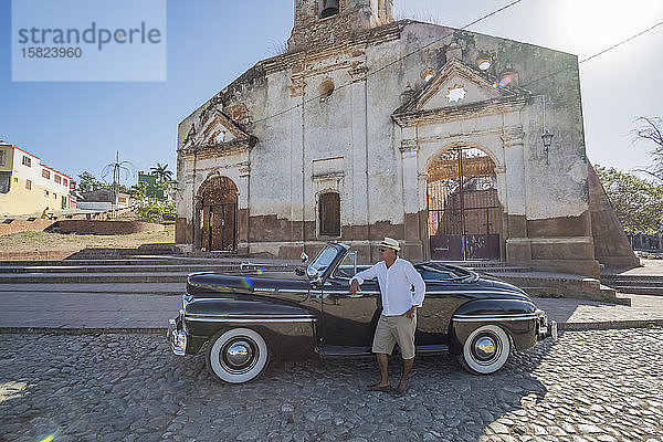 Taxifahrer,  der neben einem Oldtimer-Cabriolet steht,  Trinidad,  Kuba