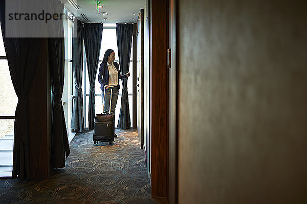 Geschäftsfrau im Hotelkorridor mit Rollkoffer