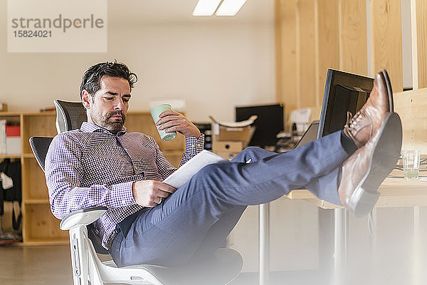 Entspannter Geschäftsmann liest Dokument am Schreibtisch im Büro
