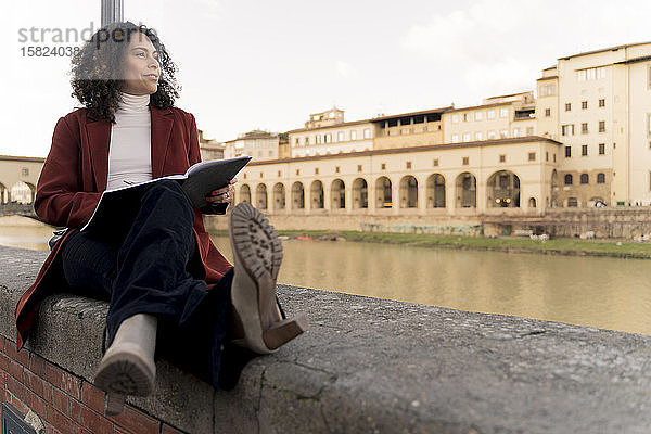 Frau sitzt auf einer Mauer am Arno,  Florenz,  Italien