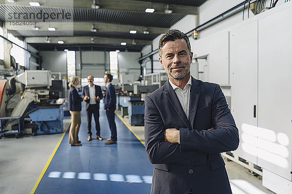 Porträt eines selbstbewussten Geschäftsmannes in einer Fabrik mit Kollegen im Hintergrund