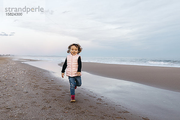 Glückliches Mädchen rennt bei Sonnenuntergang am Strand