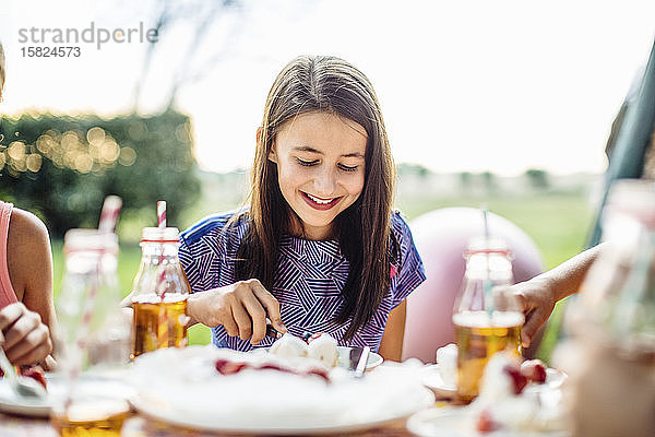 Glückliches Mädchen isst ein Stück Kuchen auf einer Geburtstagsfeier im Freien