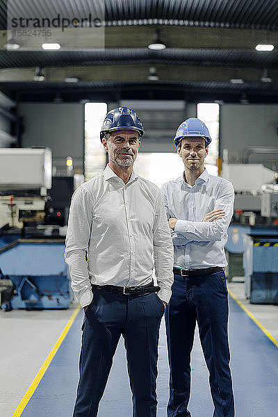 Porträt von zwei selbstbewussten Männern mit Schutzhelmen in einer Fabrik