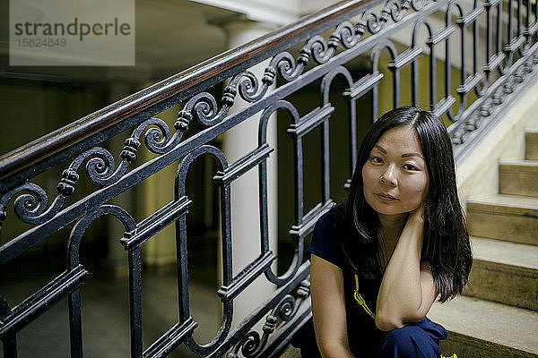 Porträt einer ernsten Frau,  die auf einer Treppe in einem alten Gebäude sitzt