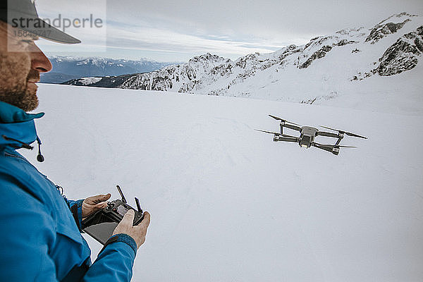 Mensch bedient Drohne auf schneebedecktem Berg.