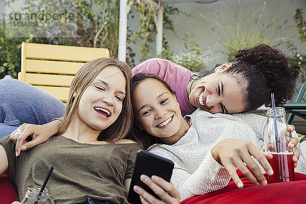 Drei Frauen,  die zusammen faulenzen,  lachen und auf ein Mobiltelefon schauen.