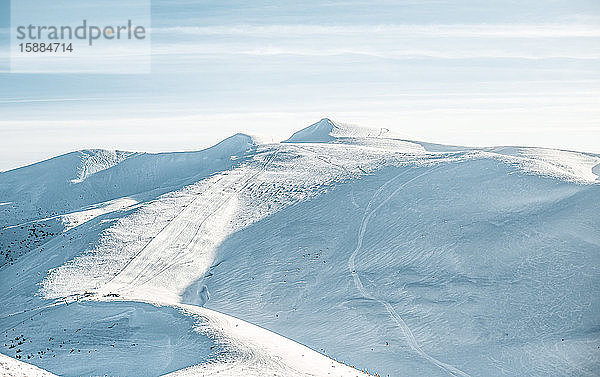 Blick auf menschenleere Skipisten in den Bergen,  leere Pisten mit Schneespuren.