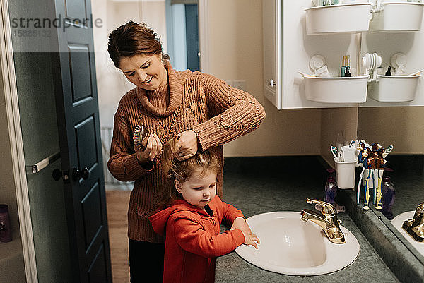 Eine Frau bürstet ihren Töchtern die Haare,  während sie im Badezimmer steht.