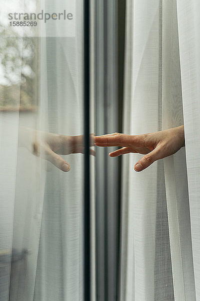 Hand einer Frau,  die eine Fensterscheibe berührt