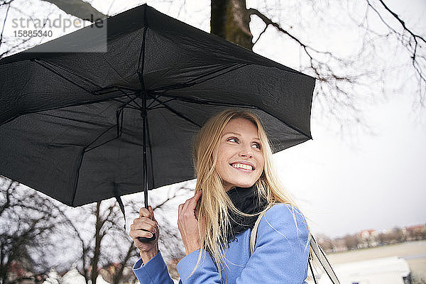 Lächelnde blonde Frau hält Regenschirm im Freien