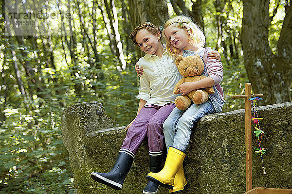 Kinder sitzen auf einer Steinmauer im Wald