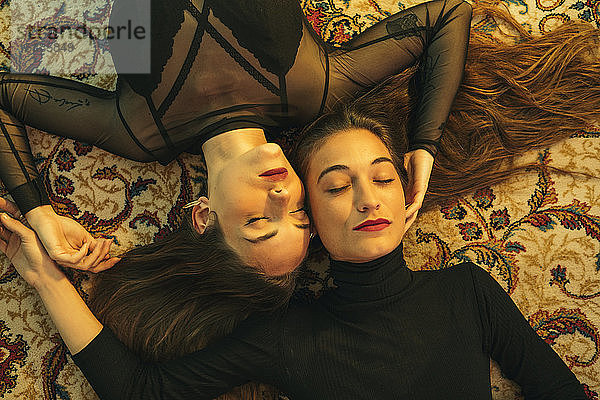 Porträt von zwei jungen Frauen,  die Kopf an Kopf auf dem Boden liegen