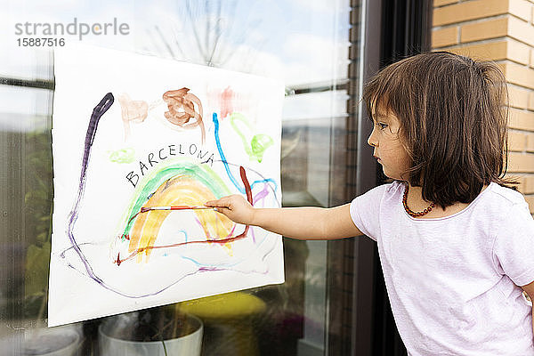 kleines Mädchen,  das ein Bild auf das Fenster malt