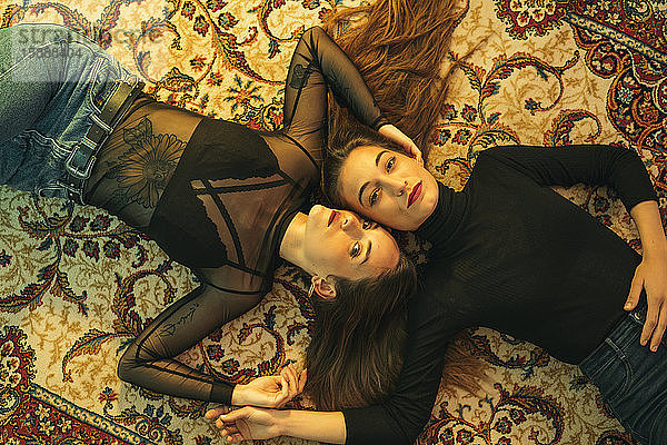 Porträt von zwei jungen Frauen,  die Kopf an Kopf auf dem Boden liegen