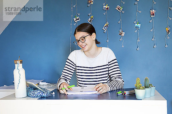 Porträt eines lächelnden Mädchens,  das zu Hause am Schreibtisch sitzt und auf ein digitales Tablet schaut