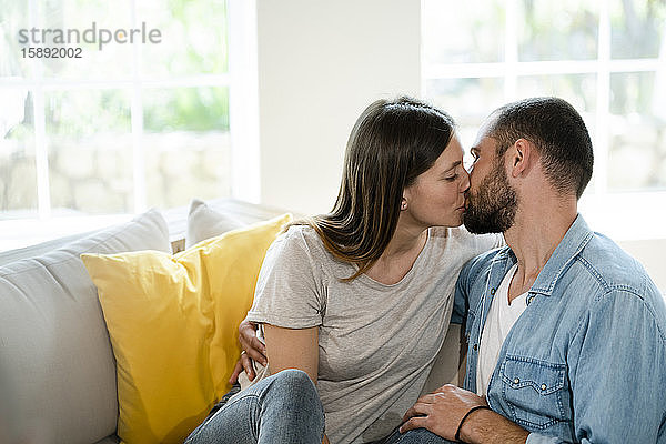 Zärtliches junges verliebtes Paar,  das sich zu Hause auf der Couch küsst