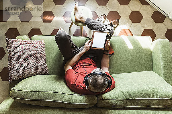 Reifer Mann sitzt auf dem Sofa und benutzt ein Tablett,  hört Musik