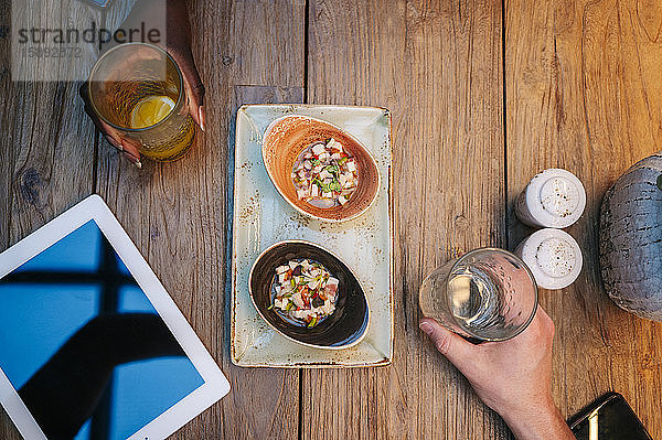 Zwei Personen sitzen im Restaurant,  essen und trinken,  mit digitalem Tablett auf dem Tisch