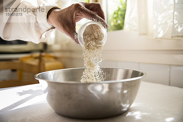 Hand einer Frau gießt Mehl in eine Schüssel
