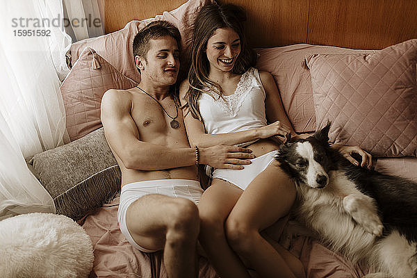 Glückliches junges Paar und Hund liegen im Bett