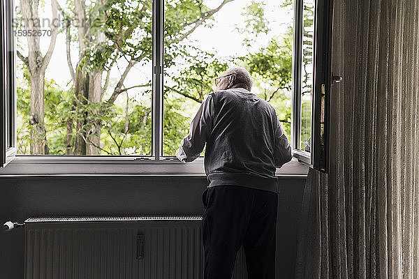 Rückenansicht eines älteren Mannes,  der aus dem Fenster schaut