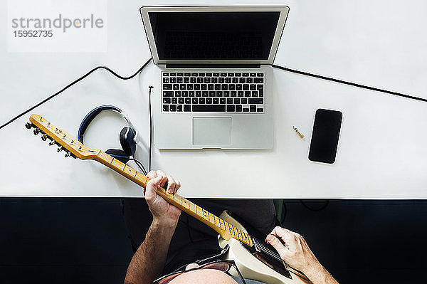 Draufsicht auf einen Mann,  der mit einem Laptop online E-Gitarre lernt