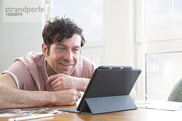 Porträt eines lächelnden Mannes mit Tablette auf dem Tisch zu Hause