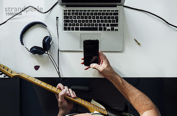 Draufsicht auf einen Mann,  der mit Laptop und Smartphone online E-Gitarre lernt