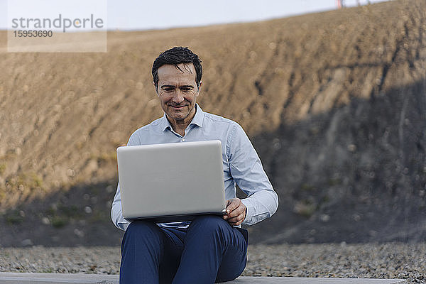 Reifer Geschäftsmann benutzt Laptop auf einer stillgelegten Minendeponie