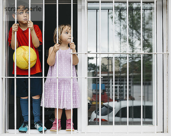 Kinder stehen am offenen Fenster am Fenstergitter