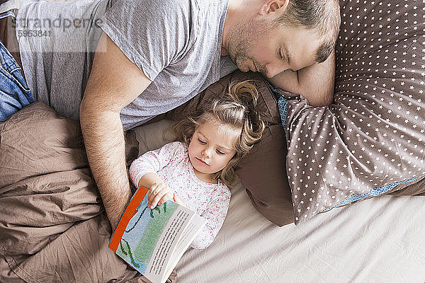 Vater und Tochter lesen ein Buch im Bett