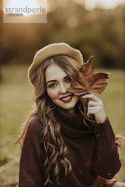 Porträt einer modischen Frau mit Herbstblatt im Gegenlicht