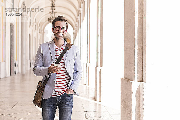 Porträt eines lächelnden jungen Mannes mit Smartphone in der Stadt,  Lissabon,  Portugal
