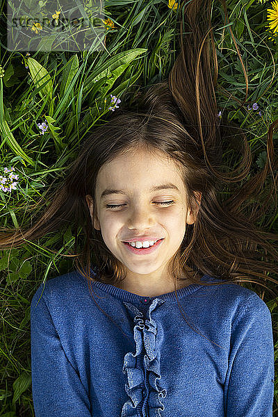 Porträt eines Mädchens mit geschlossenen Augen,  das sich im Frühling auf einer Wiese entspannt