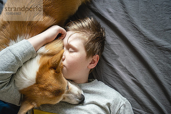 Porträt eines Jungen,  der auf dem Bett liegt und seinen Hund kuschelt